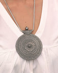 Silver necklace with intricate design worn by a person in a white dress